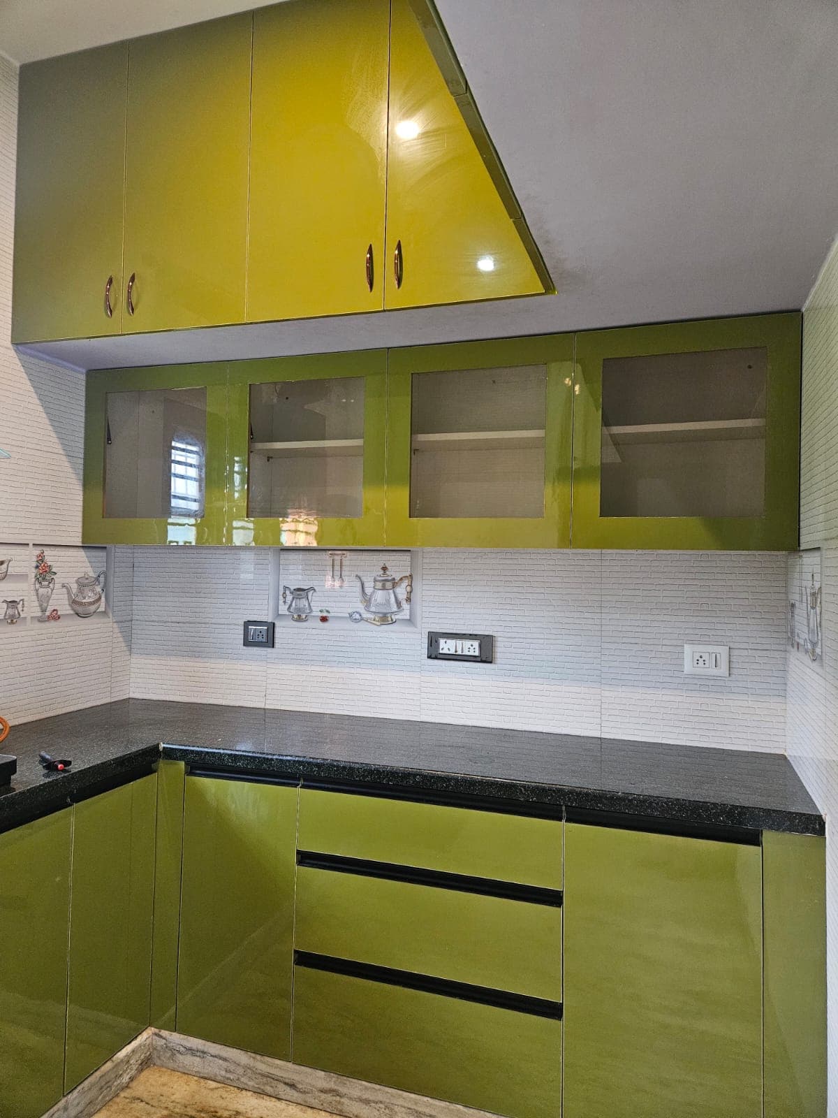 Glass-fronted wall units and drawer bank in an olive-green high-gloss modular kitchen